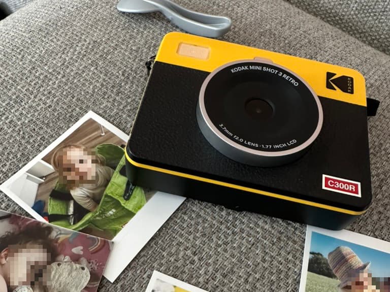 A Kodak camera that is yellow and black, below it are some photos that have been printed with it showing some children
