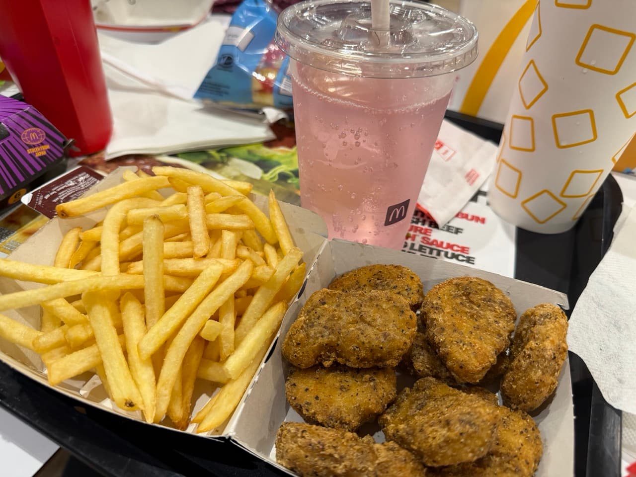 A tray with McDonalds food on it. There is a box with fries on one side and nuggets on the other. Behind that is a clear cup and straw with a pink drink in it.