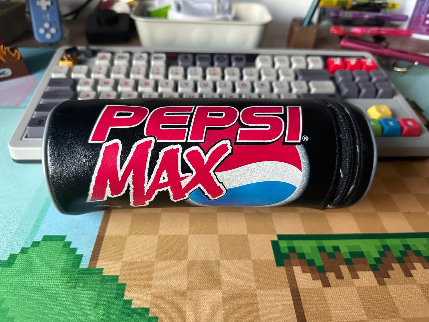 A black Pepsi Max pencil case in front of a keyboard on a desk