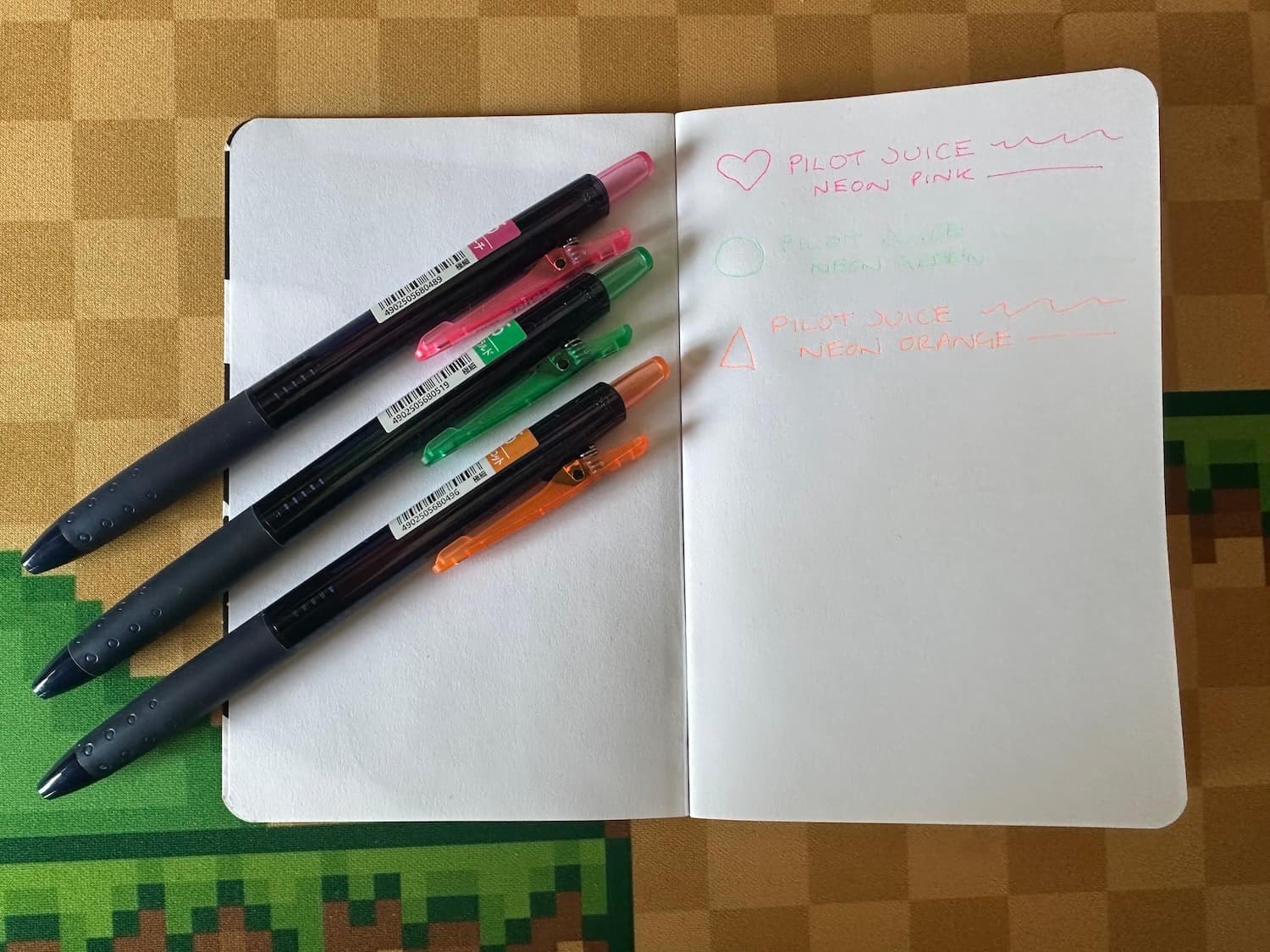 A blank notepad with samples of three neon pens which are on the left hand page