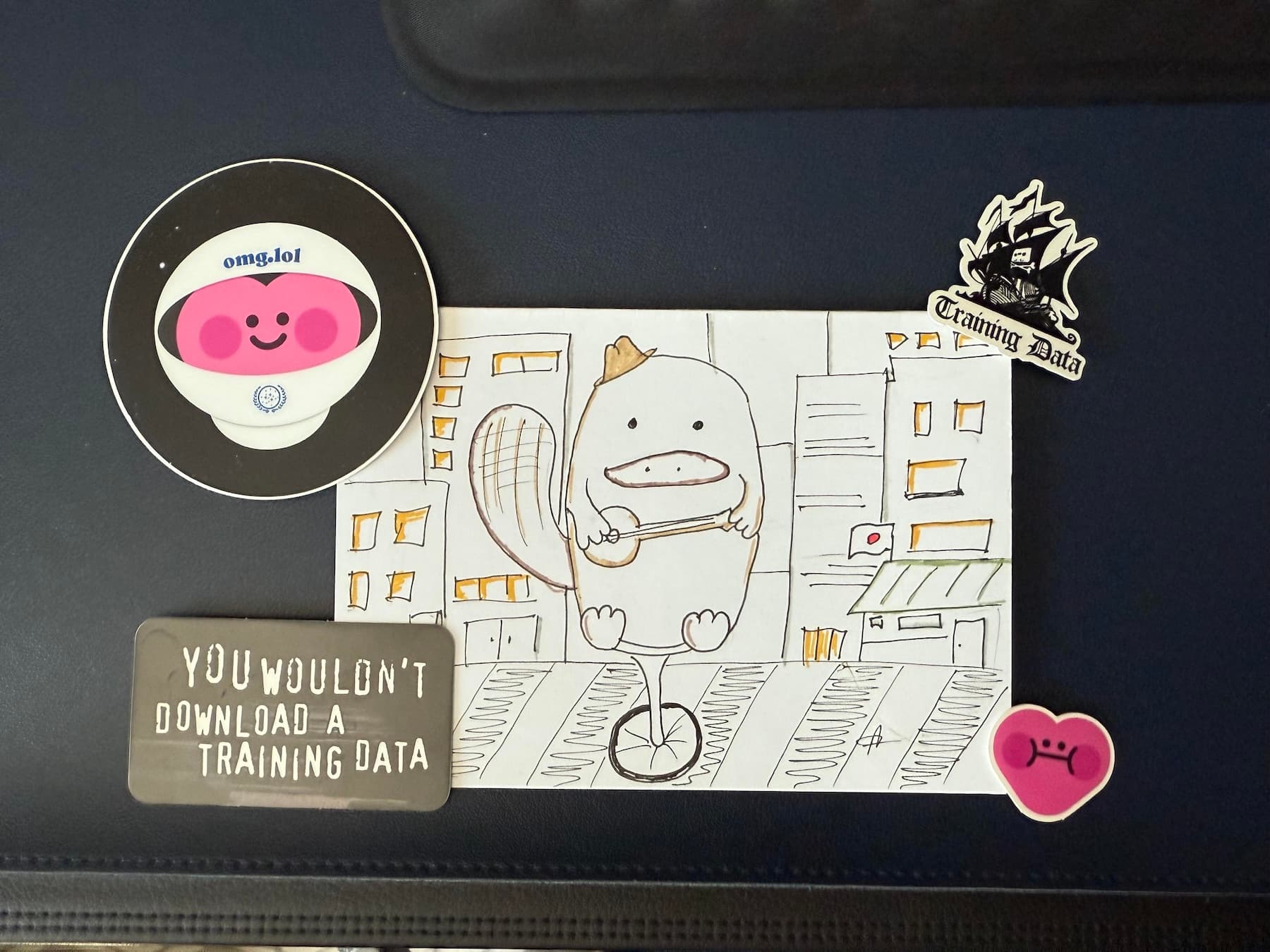 A drawing of a platypus wearing a tiny fedora and playing a banjo while sitting on a unicycle in the middle of a bustling Tokyo crosswalk at rush hour. Around it are some stickers.