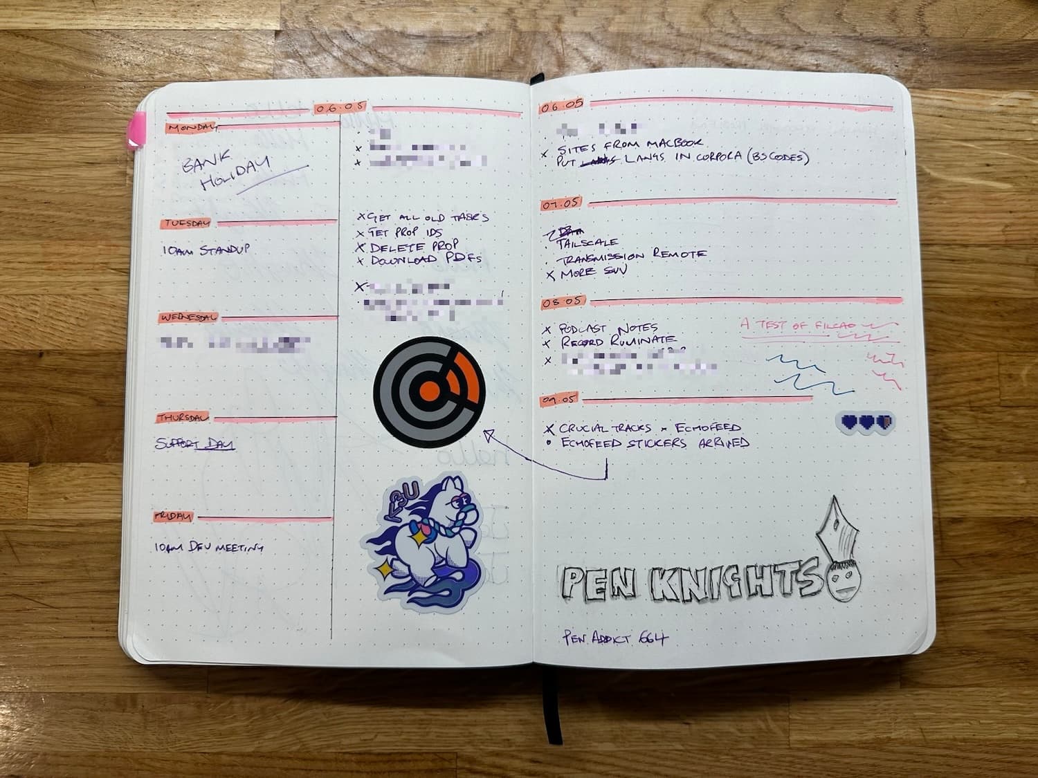 An open notebook on a wooden tabletop showing a layout for work on the left and dates on the right. There are stickers and doodles in it.