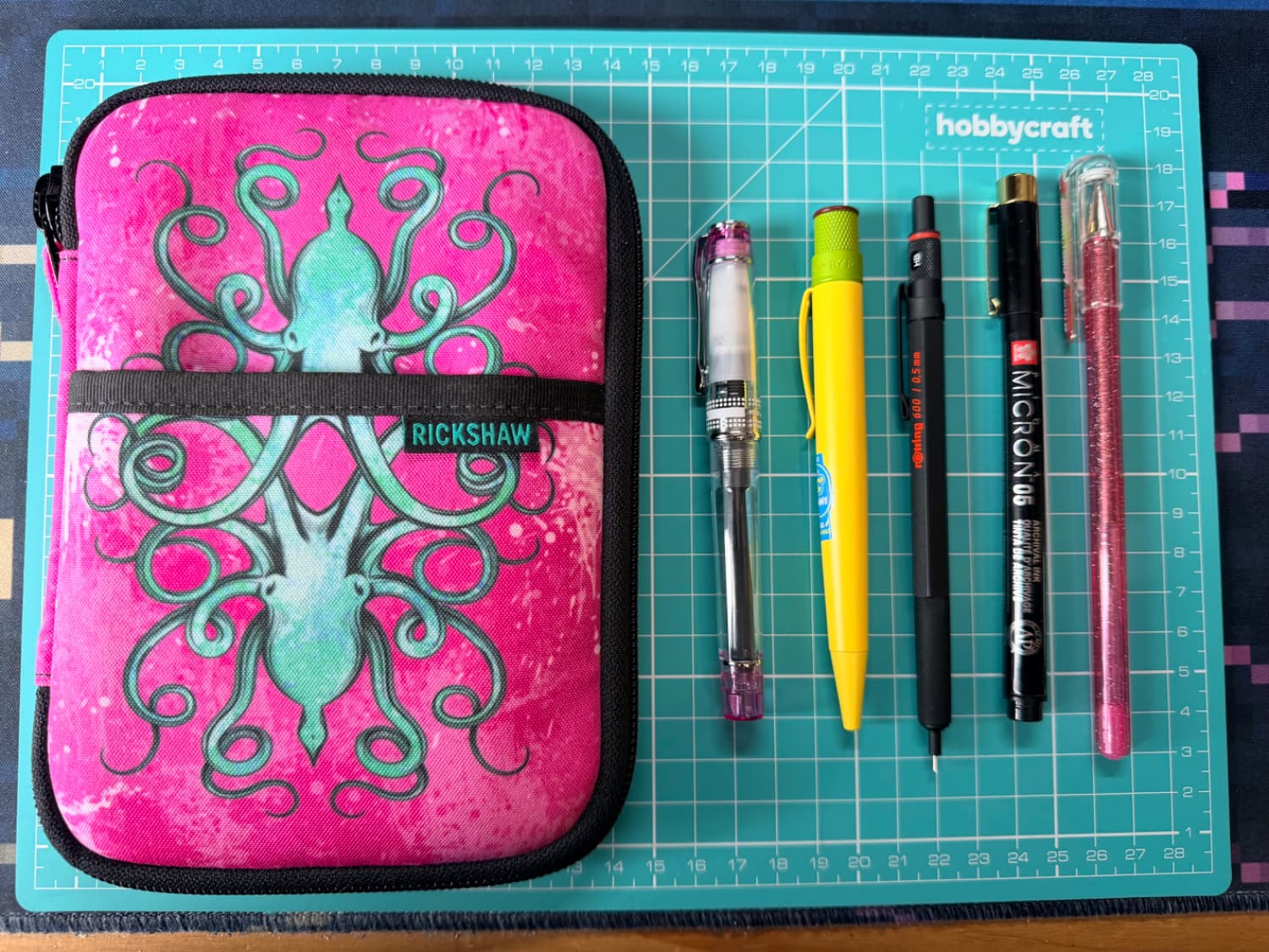 A pink pen case with an Octopus on it and next to it are some pens all lined up vertically