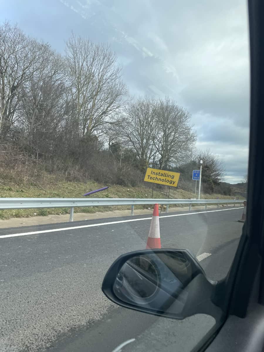 A photo taken on a motorway from a car. A road sign on the side of the road says Installing Technology