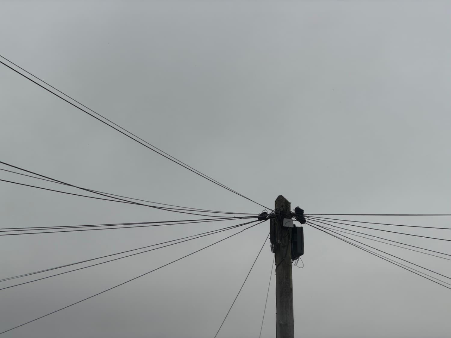 A telephone pole with wires coming out of it on a grey sky