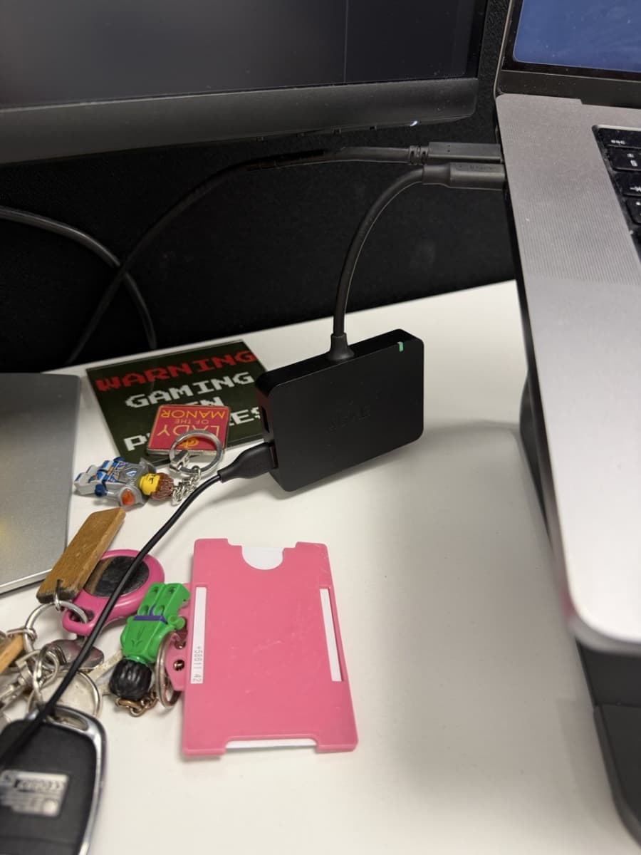 A desk showing a black USB hub with another black cable coming out of it. There are keys on the desk