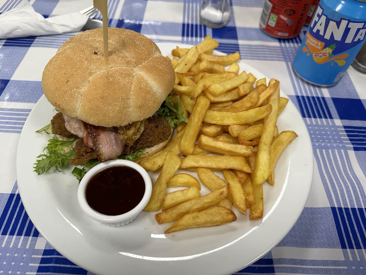 A burger and chips on a plate with a pot of BBQ sauce