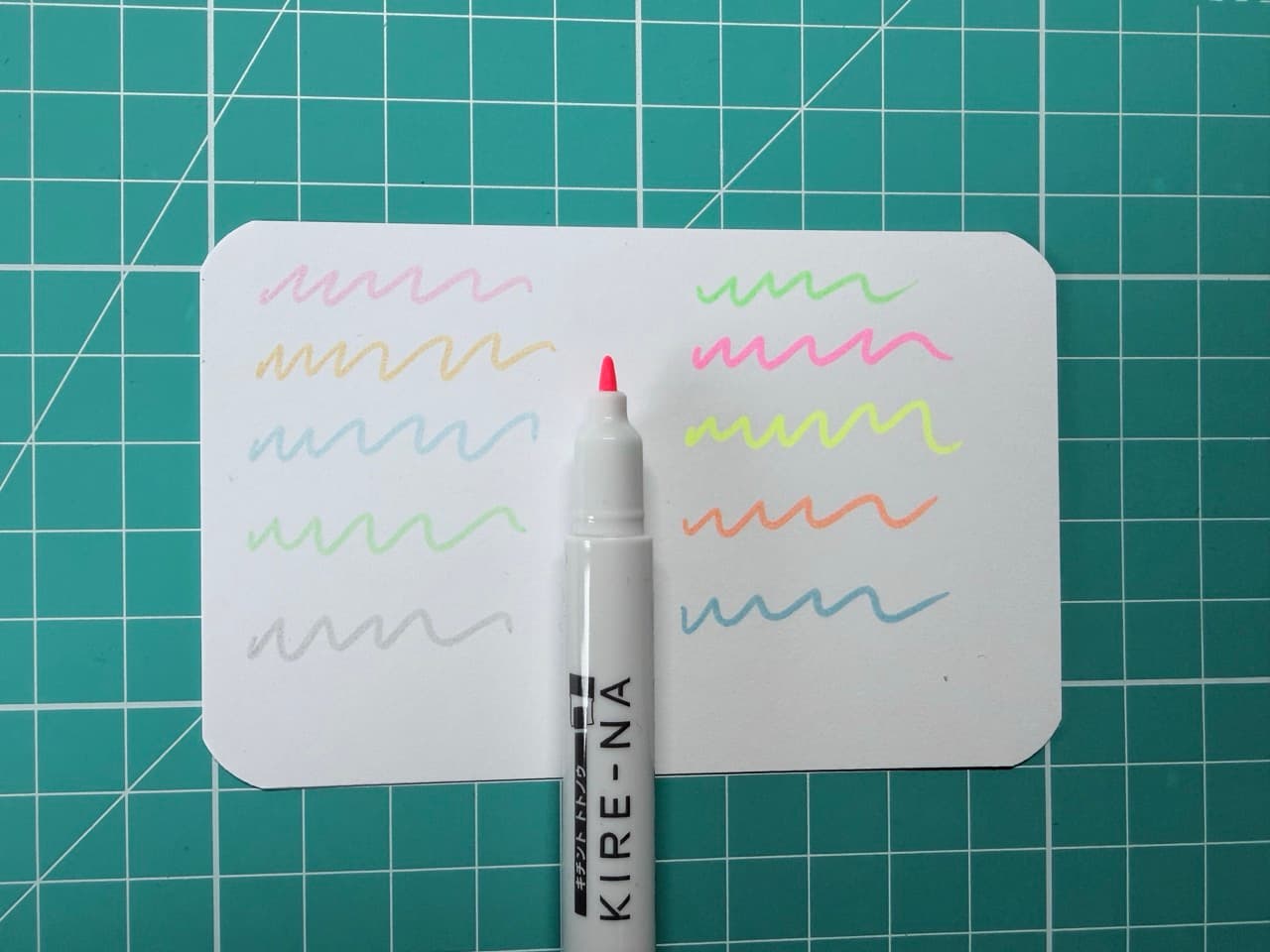 一张索引卡片,上面列出了Kire-na系列钢笔的十种颜色样本。中间是亮粉色钢笔的笔尖。