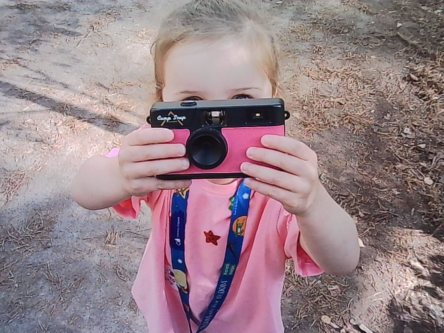 A child holding a pink camera in front of their face