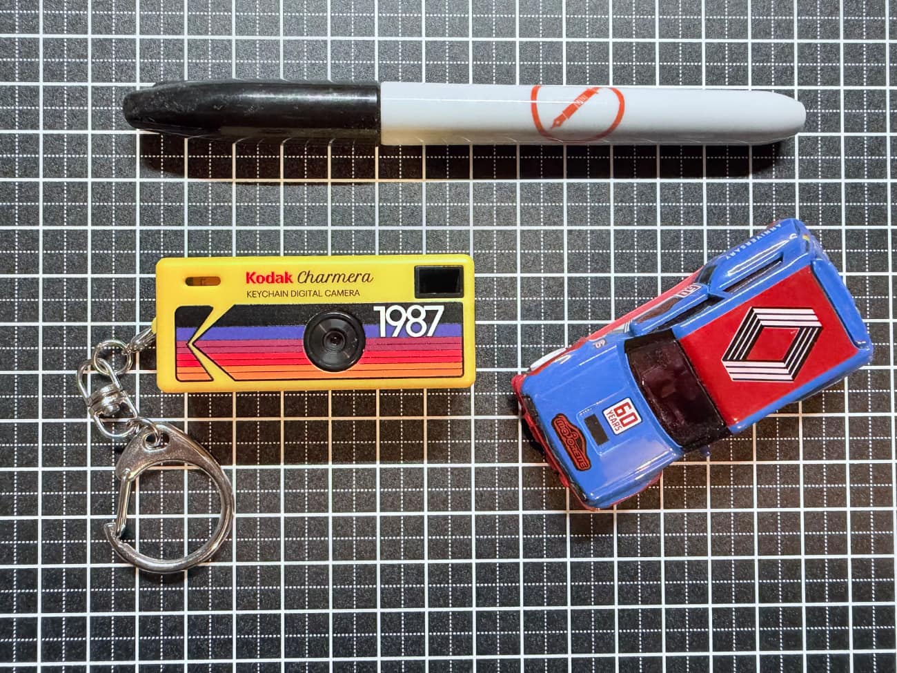 A small keyring camera next to a toy car and a sharpie
