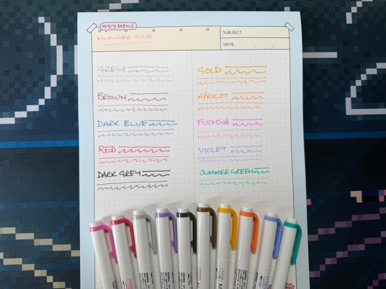 一个记事本上展示了10种不同的Mildliner荧光笔样品。所有笔都放在记事本底部。