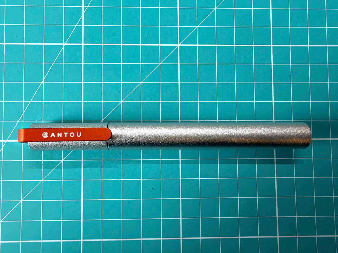 A silver pen with an orange clip on a green cutting board